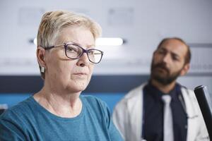 Nahansicht von ein Alten geduldig Ausbildung mit Sport Ausrüstung und Rehabilitation Gang. Porträt von alt Frau mit Brille unterziehen Physiotherapie mit Fachmann männlich Arzt. foto