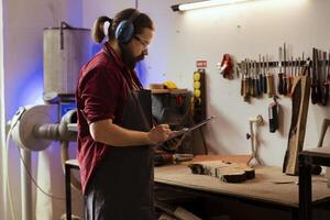 Zimmermann tragen Sicherheit Brille Zeichnung Blaupausen auf Notizblock zu machen kreativ Holz Kunst Stücke. Handwerker suchen beim technisch Schema zu ausführen Holzbearbeitung Projekte, mit schützend Ausrüstung foto