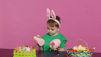 klein zufrieden Kind präsentieren versteckte handgemacht Ornamente erstellt im Vorbereitung von Ostern Urlaub Feier. jung Junge mit Hase Ohren zeigen gemalt Dekorationen, ein Hase und ein Ei. Kamera a. foto
