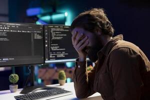 beunruhigt Mann sich ins Gesicht fassen selbst während tun Software Qualität Sicherheit, finden Haupt Fehler im Quelle Code. deprimiert Entwickler verärgert nach inspizieren Codierung auf Desktop pc und Sehen viele Probleme foto