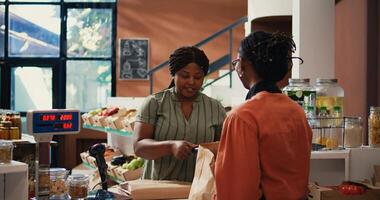 afrikanisch amerikanisch Klient bezahlen zum organisch Essen mit Karte, Kauf ethisch bezogen bio Früchte und Gemüse mit pos Zahlung beim Supermarkt Kasse. Frau Einkauf produzieren. Handheld Schuss. foto