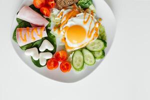 elegant Teller von gebraten Eier dekoriert mit frisch Spinat Blätter und Gemüse auf eben Weiß Platte. Makro Foto von gesund nahrhaft Frühstück isoliert auf Weiß Hintergrund