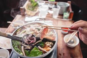 heiß Topf mit klar Suppe, Schweinefleisch, Fisch, Gemüse, blanchiert im heiß Brühe und eingetaucht im ein Vielfalt von Saucen. foto