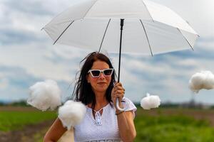 Frau ist halten ein Weiß Regenschirm und umgeben durch Baumwolle Wolken foto