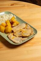 ein saftig geröstet Schweinefleisch Lende sitzt auf ein Teller neben goldbraun geröstet Kartoffeln und ein Hügel von flauschige Weiß Reis. das Gericht ist vorgestellt im ein gemütlich Restaurant foto