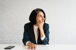 junge kaukasische brünette geschäftsfrau direktorin im büro schauen zur seite des leeren raums, der nachdenklich ist, treffen entscheidungen im büro allein am arbeitstisch foto