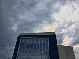 ein Büro Gebäude mit Blau Wände und ein Fassade gemacht von Glas Das spiegelt das Wolken und Himmel foto