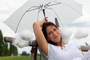 Frau ist halten ein Weiß Regenschirm und umgeben durch Baumwolle Wolken foto