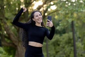 lächelnd, aktiv weiblich im sportlich Kleidung erfasst ein heiter Moment auf ihr Telefon, verkörpern Gesundheit und Glück. foto