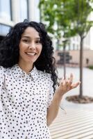 heiter jung Frau haben ein Anruf während Gehen Nieder das Straße, chatten mit Freunde, nehmen ein Selfie, suchen beim das Kamera. foto