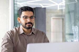 konzentriert indisch Geschäftsmann mit ein Laptop beim seine Büro Arbeitsplatz, verkörpern Professionalität und Einsatz. foto