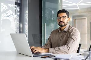 Fachmann indisch Geschäftsmann im ein modern Büro Arbeiten aufmerksam auf ein Laptop, porträtieren Vertrauen und Einsatz. foto