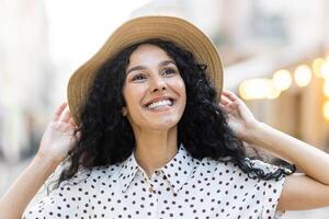 Nahansicht Porträt von ein glücklich Mit freundlichen Grüßen lächelnd jung spanisch Mädchen Gehen im das Stadt im sonnig Wetter im ein groß Hut, sorglos Leben, Tourist gehen. foto