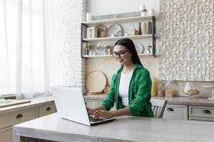 junge schöne Geschäftsfrau mit Brille und grünem Hemd, die zu Hause in der Küche arbeitet foto