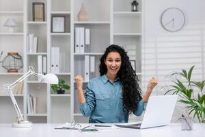 froh spanisch Frau Arbeiten von heim, ausdrücken Erfolg und Glück im ein schön organisiert Büro Raum. foto