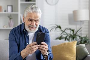 glücklich Senior Gentleman lächelnd während Surfen durch seine Smartphone, bequem sitzend auf ein Sofa im ein gut beleuchtet Leben Zimmer. foto