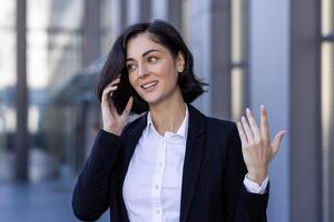 jung erfolgreich zufrieden Geschäft Frau reden auf das Telefon, weiblich Arbeiter im ein Geschäft passen Gehen um das Stadt draußen ein Büro Gebäude. foto