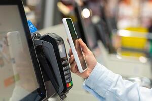 Nahansicht Frau Zähler Kaufen elektronisch Zahlung Supermarkt Smartphone weiblich Hand mit ein Handy, Mobiltelefon Telefon im Zahlen zum Einkäufe im Shops kontaktlos nfc Terminal Nahansicht Karte Leser foto