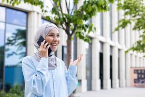 jung froh Geschäftsfrau im Hijab reden auf das Telefon draußen ein Büro Gebäude. foto