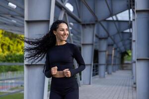 jung schön spanisch Frau mit lockig Haar Joggen in der Nähe von Stadion, Frau im Trainingsanzug lächelnd zufrieden, Laufen im Park. foto