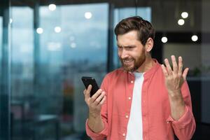 Geschäftsmann im rot Hemd empfangen Schlecht Nachrichten Botschaft online Botschaft auf Telefon, reifen Mann lesen von online Anwendung Innerhalb Büro Arbeitsplatz Stehen in der Nähe von Fenster. foto