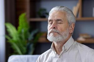 ein heiter Porträt von ein grauhaarig Senior Mann meditieren mit geschlossen Augen, Sitzung bequem im seine gut dekoriert Leben Zimmer mit beschwingt Grün Pflanzen. foto