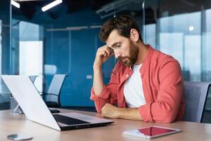 frustriert Geschäftsmann deprimiert beim Arbeitsplatz Arbeiten auf Laptop, Mann im Hemd verärgert und traurig unzufrieden mit Schlecht Arbeit Ergebnisse und Leistung Innerhalb Büro. foto