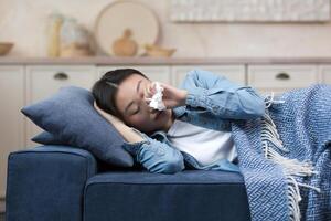 Nahansicht Foto von ein krank Frau Lügen auf das Sofa beim heim, haben ein Fieber und Grippe, ein asiatisch Frau Lügen unter ein Decke auf das Sofa