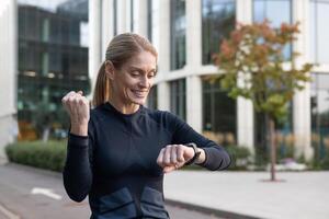 ein passen Frau mit ein Lächeln prüft ihr Fitness Tracker draussen, ausströmend Glück und ein gesund Lebensstil. mit ein Hintergrund von städtisch die Architektur, diese Bild erfasst das Wesen von aktiv Leben im das Stadt. foto