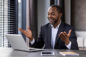 erfolgreich reifen Boss im Geschäft passen Innerhalb Büro mit Laptop, reden entfernt mit Forderung, Mann lächelnd gestikulieren befriedigt, Geschäftsmann Investor beim arbeiten. foto