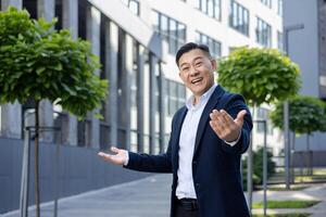 zuversichtlich asiatisch Geschäftsmann im passen begrüßt mit ein Handschlag Geste, Stehen draußen ein modern Büro Gebäude. foto