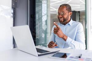 reifen afrikanisch amerikanisch Boss Arbeiten Innerhalb Büro mit Laptop aus der Ferne, Geschäftsmann im Hemd auf online Treffen mit Kollegen, Mann reden auf Anruf mit Laptop während Sitzung im Shirt. foto