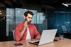 Büro Arbeiter hat ein Zahnschmerzen, ein krank Geschäftsmann funktioniert Innerhalb das Büro mit ein Laptop, ein Mann hat ein Zahnschmerzen beim das Arbeitsplatz. foto