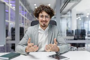 beschäftigt, verlobt jung Fachmann mit lockig Haar diskutieren Ideen beim seine Büro Arbeitsplatz, verkörpern korporativ Begeisterung und Sachverstand. foto