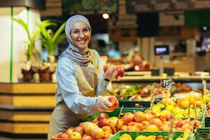 ein jung schön Hijabi Muslim Frau, ein Supermarkt Arbeiter, liegt Obst im das Abteilung foto