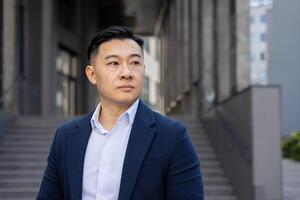 ein Fachmann asiatisch Geschäftsmann draußen im ein Stadt Umfeld, Blick nachdenklich mit Vertrauen. foto