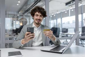 lockiges Haar jung Geschäftsmann im ein modern Büro Multitasking mit ein Laptop und Smartphone, vorbildlich konzentriert korporativ arbeiten. foto