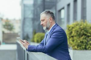 ein brechen beim arbeiten. ein älter männlich Geschäftsmann ist Stehen auf das Balkon von ein Büro Center mit ein Tablette im seine Hände. Zifferblätter, liest Nachricht, liest, ruht. foto