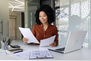 jung erfolgreich Financier funktioniert mit Unterlagen und Verträge Innerhalb das Büro, zufrieden mit das Ergebnisse von finanziell Aktivitäten, Geschäftsfrau Bewertungen Konten, Berichte und Verträge, Laptop. foto