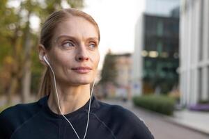 Nahansicht von ein entschlossen weiblich Läufer mit Kopfhörer Hören zu Musik- während Joggen durch ein städtisch Einstellung, vorbildlich ein gesund, aktiv Lebensstil. foto
