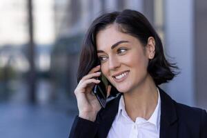 jung erfolgreich zufrieden Geschäft Frau reden auf das Telefon, weiblich Arbeiter im ein Geschäft passen Gehen um das Stadt draußen ein Büro Gebäude. foto