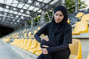 ein Frau halten ihr Knie im Schmerzen während sitzend auf Stadion Schritte, vorschlagen ein sportbezogen Knie Verletzung. foto
