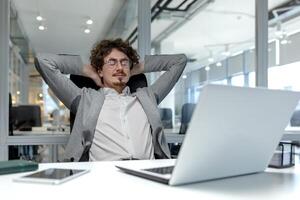 ein jung Geschäftsmann mit lockig Haar entfaltet sich im ein modern Büro, zeigen ein Moment von Entspannung inmitten ein beschäftigt korporativ Einstellung. foto