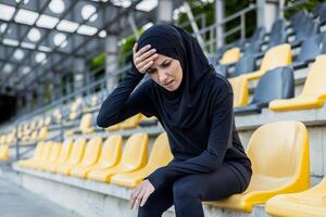 ein müde weiblich Athlet im Hijab Sitzung auf Stadion Sitze, zeigen Zeichen von ermüden und Erschöpfung nach Ausbildung. foto