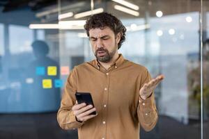 reifen Mann mit ein verwirrt Ausdruck Überprüfung seine Smartphone. Büro Rahmen mit verschwommen Hintergrund. foto