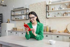 ein jung Frau Sitzung im das Küche und mit das Telefon. Getränke Kaffee,, Typen Mitteilungen foto