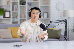 ein einnehmend asiatisch Mann reden und suchen beim das Kamera während Aufzeichnung ein Podcast im ein Zuhause Studio Einstellung. foto