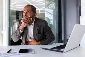 krank Mann beim Arbeitsplatz Innerhalb Büro, afrikanisch amerikanisch Mann habe Essen Vergiftung auf Mittagessen brechen, Geschäftsmann hat Übelkeit und rülpst während Sitzung beim Schreibtisch. foto