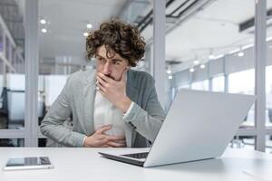 lockiges Haar männlich Fachmann Arbeiten aufmerksam auf Laptop im Büro Einstellung, ausströmend Erfahrung und Konzentration. foto