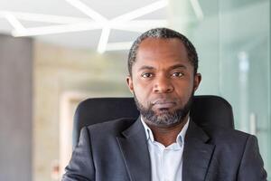 schließen oben Porträt von reifen erfahren Geschäftsmann, afrikanisch amerikanisch Mann Innerhalb Büro beim Arbeitsplatz suchen nachdenklich beim Kamera, Boss im Geschäft passen Senior Mann. foto